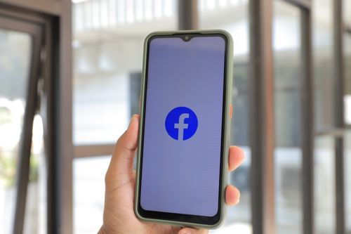 Free Close-up of smartphone with Facebook app open held by hand indoors. Stock Photo