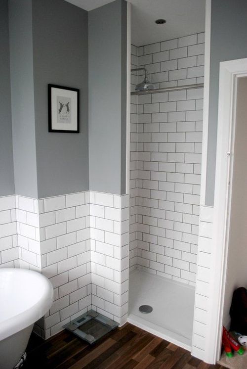 a bathroom with gray walls and white tiles on the shower wall, wood flooring