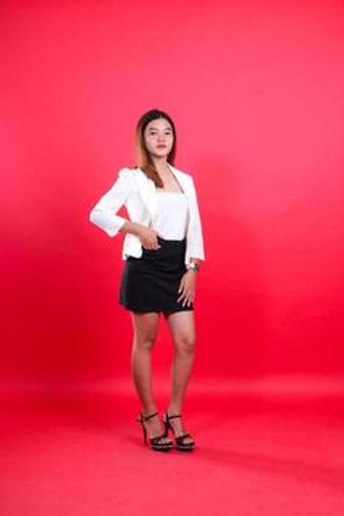 full body of beautiful young office female wearing elegant white suit with hands in skirt pocket and touching thighs, standing isolated on red background. for corporate, business, fashion content photo