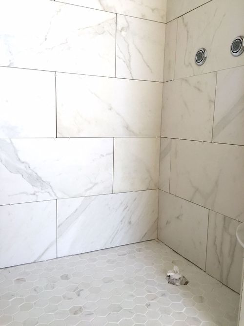 a bathroom with white marble tile and hexagonal pattern on the floor, along with a shower head