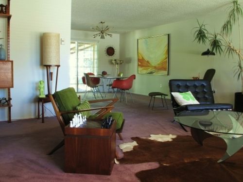 A pastel grene mid-century modern living room with dark stained furniture, potted greenery, artworks and lamps.