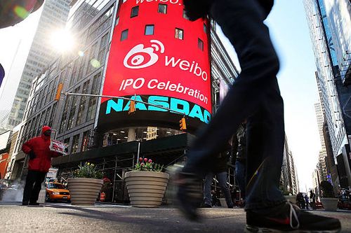 People walk by the Nasdaq exchange in Times Square moments before China's Weibo began trading on the Nasdaq exchange under the ticker symbol WB on...