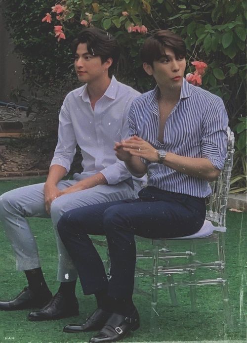 two young men sitting next to each other on top of a chair in the grass