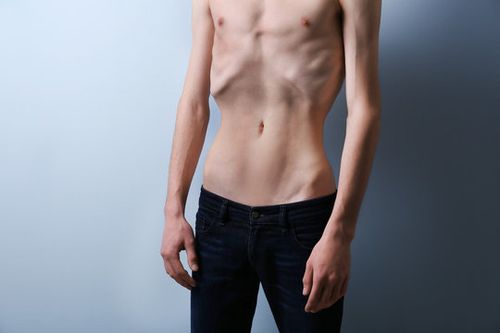 Skinny young man with anorexia on grey background