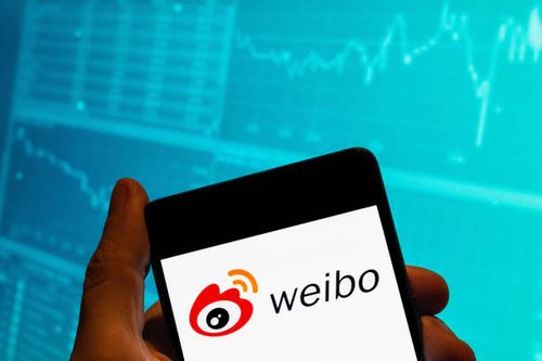 In this photo illustration, the Chinese social media platform Weibo logo is seen displayed on a smartphone with an economic stock exchange index...