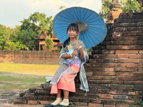 Free Young Thai girl in traditional attire holding a parasol at ancient ruins in Thailand. Stock Photo