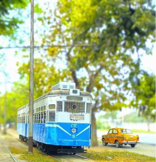 a blue and white train traveling down tracks next to a yellow car on the road