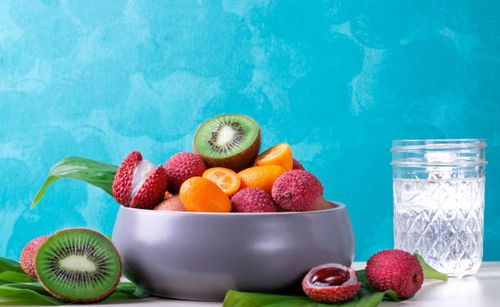 Assorted tropical fruits and water on turquoise background Lychee, kiwi and kumquat in a gray ceramic bowl and a glass of water against the turquoise background. Assorted tropical fruits. Trendy still life fruit salad glass stock pictures, royalty-free photos & images