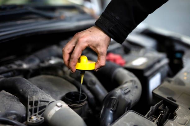 Technician checking engine oil dipstick during routine maintenance at Tuttle-Click Tustin Chrysler Jeep Dodge Ram