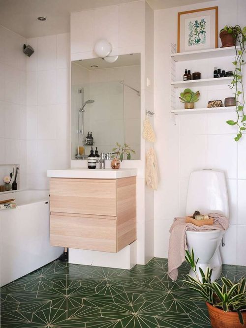 Bold green mosaic floor tiles in a simple white bathroom with a wooden vanity and lots of plants