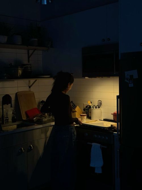 a woman standing in a kitchen at night with her hand on the stove top and lights on