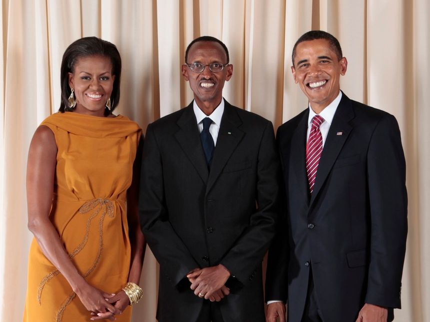 Michelle Obama, Paul Kagame and Barack Obama, standing and smiling in front of a curtain