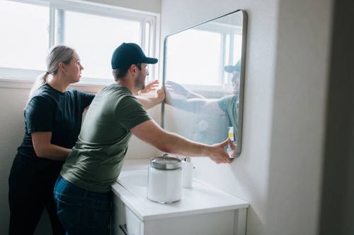 Home Remodel DIY Bathroom Improvments A Caucasian couple install a bathroom mirror in their house for a renovation project.  They take measurements to insure a proper installation. bathroom-remodeling stock pictures, royalty-free photos & images