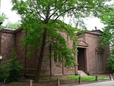 Brown stone building with classical columns and a pediment, partially obscured by leafy trees, known as the Yale Skull and Bones Society tomb.