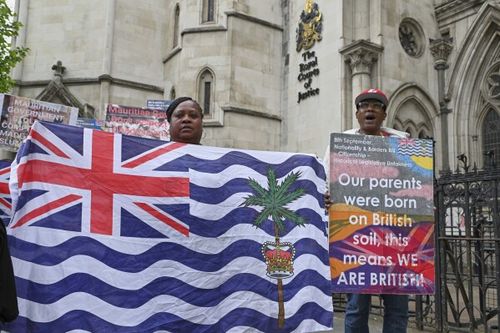 people holding up a large british and british flag in front of a building
