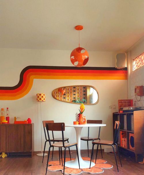 Playful retro 70s living room dining area with bold rainbow stripe mural, tulip table and vintage chairs.