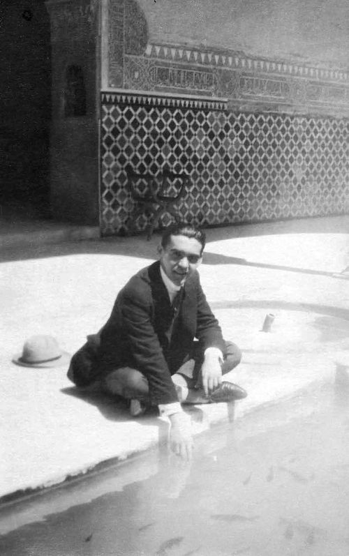 Federico García Lorca smiling, standing in front of a theatre poster