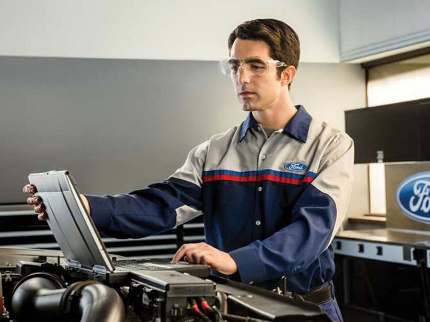 Ford technician using diagnostic computer to inspect vehicle systems at Irvine Ford service center
