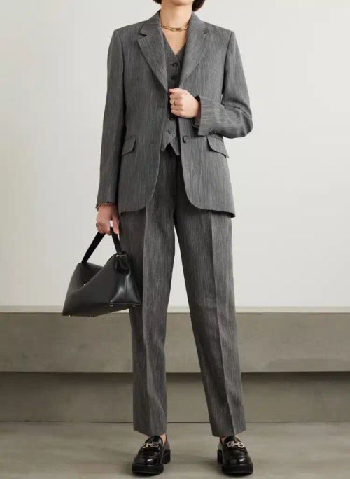 Image showing a female executive in a business professional light gray pantsuit with one hand holding a black purse and the other resting on a blazer that can be dressed down for business casual attire.