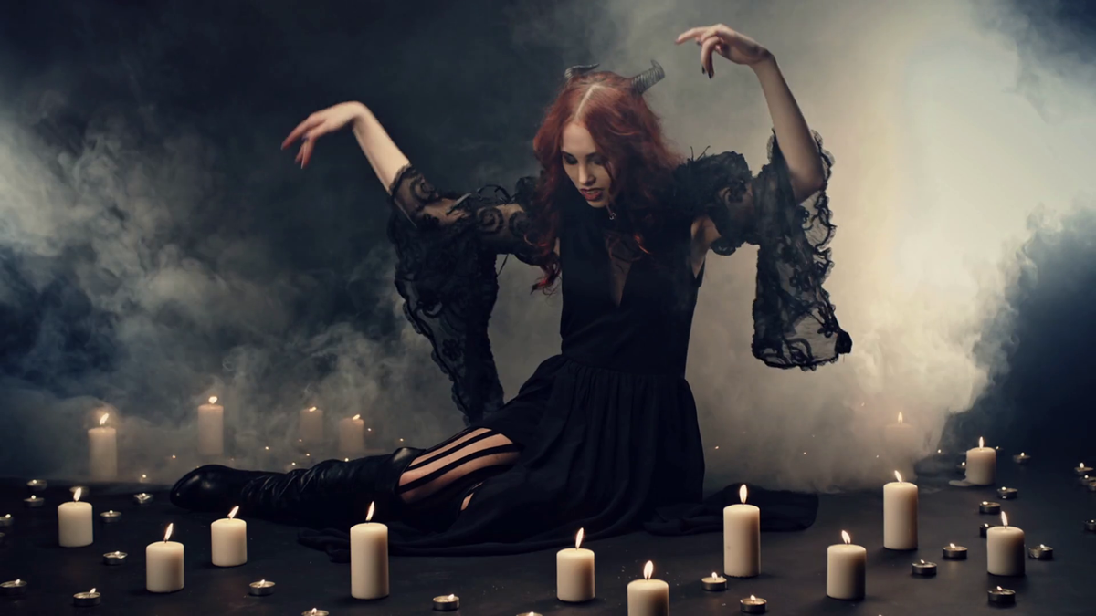 Red-haired witch sitting on floor in smoke, making energetic hand gestures to call demons ...
