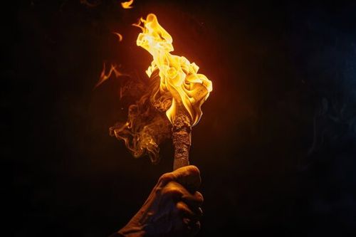 A hand holding a burning torch in the dark. Suitable for dramatic or mysterious themes