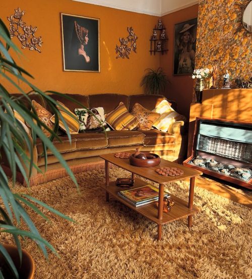 Nostalgic retro 70s living room with floral wallpapered chimney breast, velvet sofa, striped cushions and deep shag carpet.