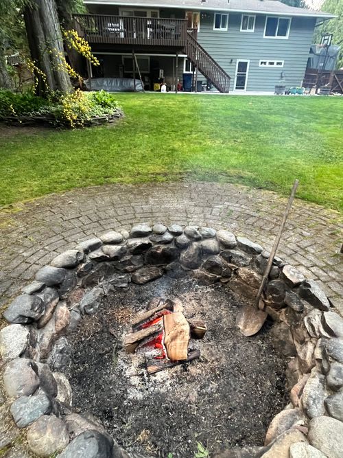 an open fire pit in the middle of a yard with rocks and grass around it