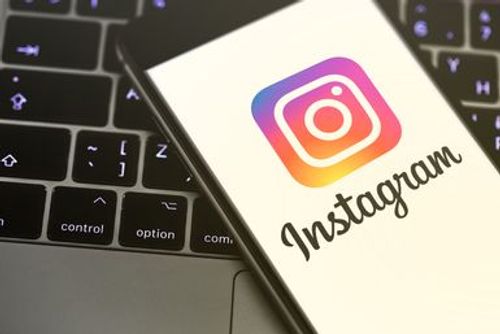 A smartphone displaying the Instagram logo and name rests on a laptop keyboard, with the screen showing the app's colorful icon and the word Instagram in script.
