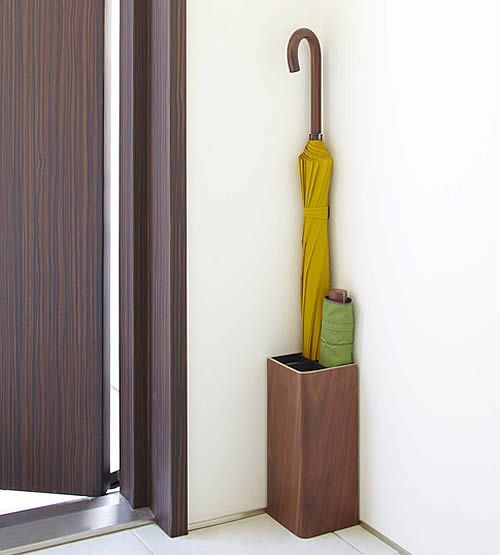 an open umbrella is sitting on the floor next to a wooden holder with two umbrellas in it