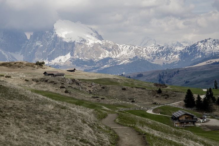 The Swiss mountain range of the Alps with a cabin sitting on a hill in the foreground.