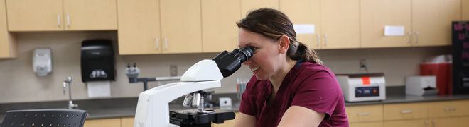 A student looks through a microscope in a classroom lab.