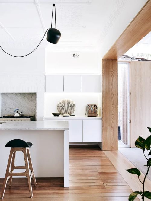 Modern kitchen with white cabinets, wooden floors, marble countertop, and a black pendant light.