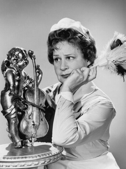 a woman leaning on a table next to a statue and holding a feather in her hand