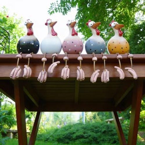 May include: Five whimsical ceramic chicken figurines with colorful bodies and red combs are perched on a wooden table. Each chicken has a unique color scheme, including black with white polka dots, white, pink with white dots, blue with white dots, and yellow with brown dots. Their legs are dangling hands.