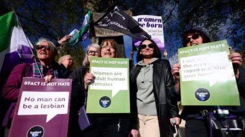 EPA Women hold flags and signs saying "women are adult human females" in an outdoor demonstration.
