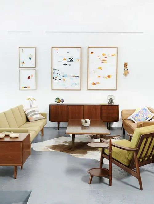 A bright mid-century modern living room with mustard colored furniture and abstract paintings.