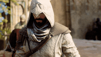 Video game gif. Basim in 'Assassin's Creed Mirage' walks towards us with a badass expression on his face, hood pulled down over his eyes as other characters move about a medieval city in the blurred background.