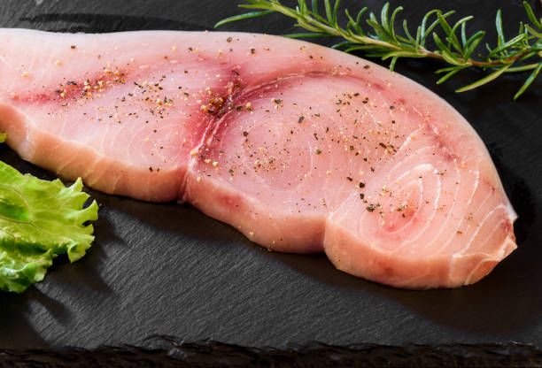 Raw Swordfish fillet covered with black pepper and with rosemary sprigs on black slate plate. Raw Swordfish fillet covered with black pepper and with rosemary sprigs on black slate plate. swordfish stock pictures, royalty-free photos & images