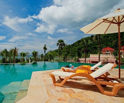 Infinity pool with sun loungers and umbrella overlooking a tropical coastline.