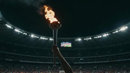 Lit torch held aloft in a packed stadium at night