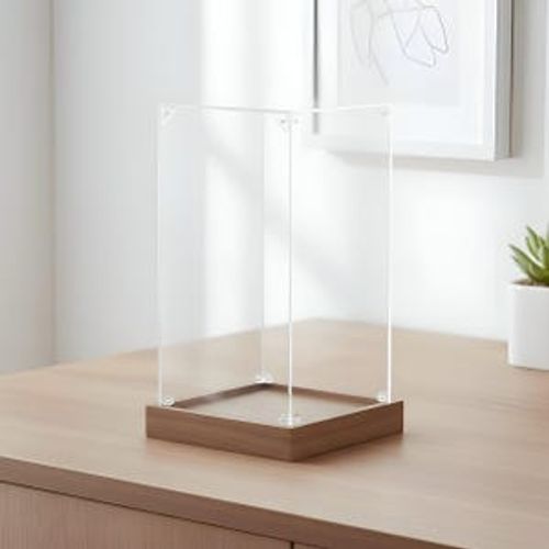 May include: A clear acrylic display case with a rectangular wooden base. The case is assembled with small, clear corner fasteners. The wooden base has a natural wood grain finish. The display case is sitting on a light-colored wooden surface.