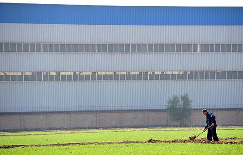 Farmer works his plot of land which runs to the edge of a recently built manufacturing and assembly factory in Tongxian county on the southern...