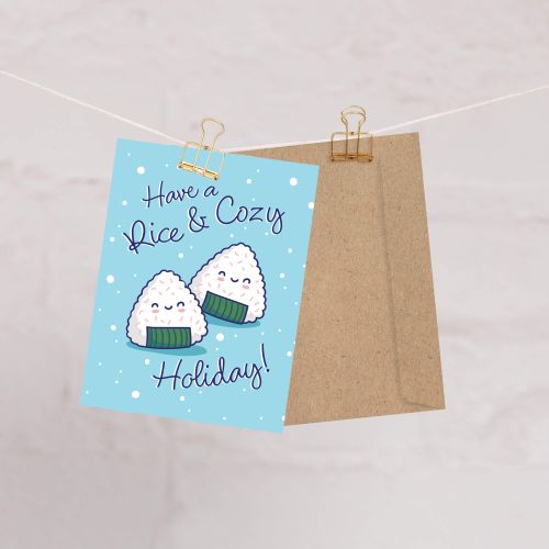 unique christmas card with Two smiling onigiri (japanese rice ball snacks) on snowy blue with text “Have a Rice & Cozy Holiday.”