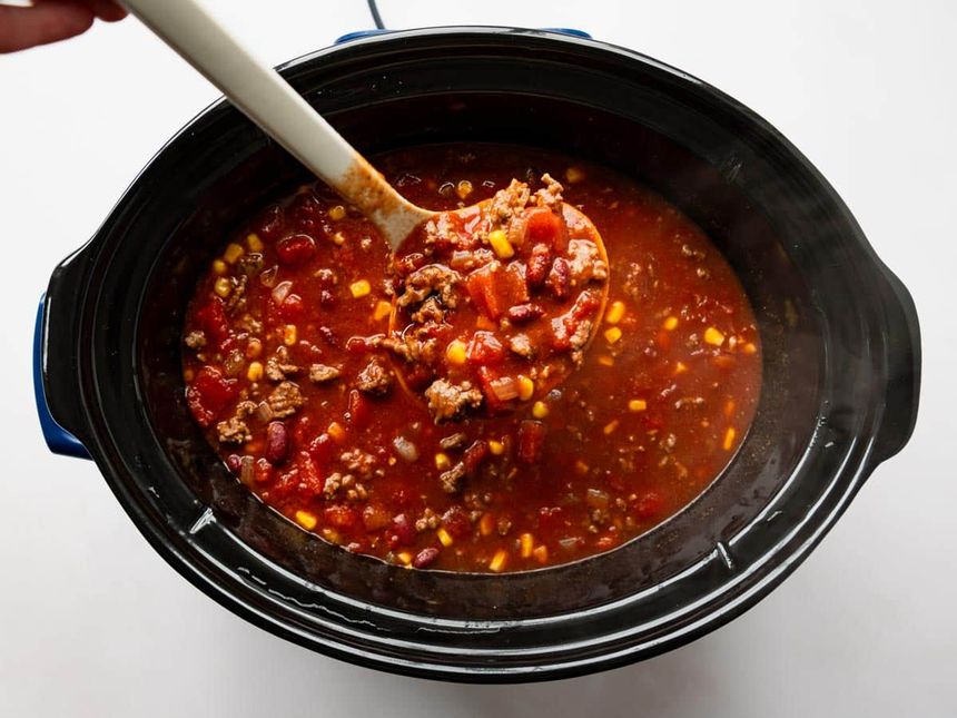 A ladle serving beef chili from a slow cooker.