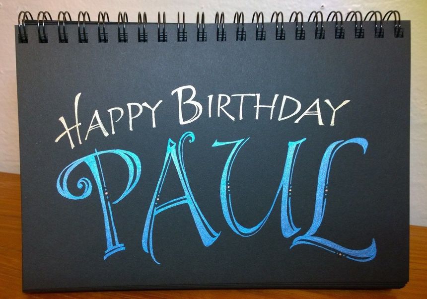 a black notebook with the words happy birthday paul written in blue ink on it, sitting on a wooden table