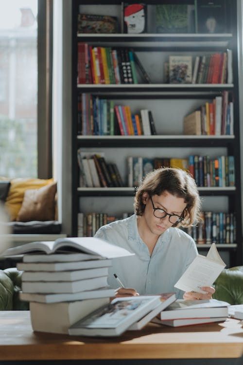 Free A young man focuses on studying amidst a bookstore environment, surrounded by books. Stock Photo