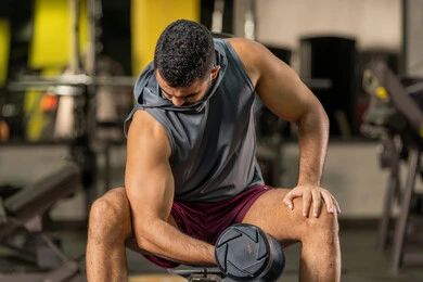 رياضة كمال الأجسام، استخدام الاثقال الرياضية، شاب عربي خليجي اماراتي يرتدي الزي الرياضي يقوم بممارسة تمارين رفع الأوزان، رجل سعودي يحمل بيده الدامبلز، الاهتمام بالصحة واللياقة الجسدية، إيماءات القوة والعزم، بناء الكتلة العضلية للجسم