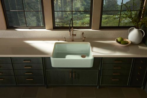 Farmhouse-style white apron sink under a large window with a bronze faucet and neutral countertops
