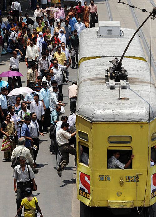 Indian commuters jump onto a government-run tram while others wait for transport at a bus stand in Kolkata on July 24, 2009. The operators of...
