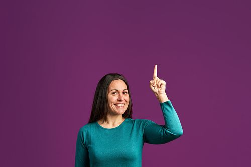 成年女子指着一个拷贝空间，同时看着相机对着紫色的背景图片下载